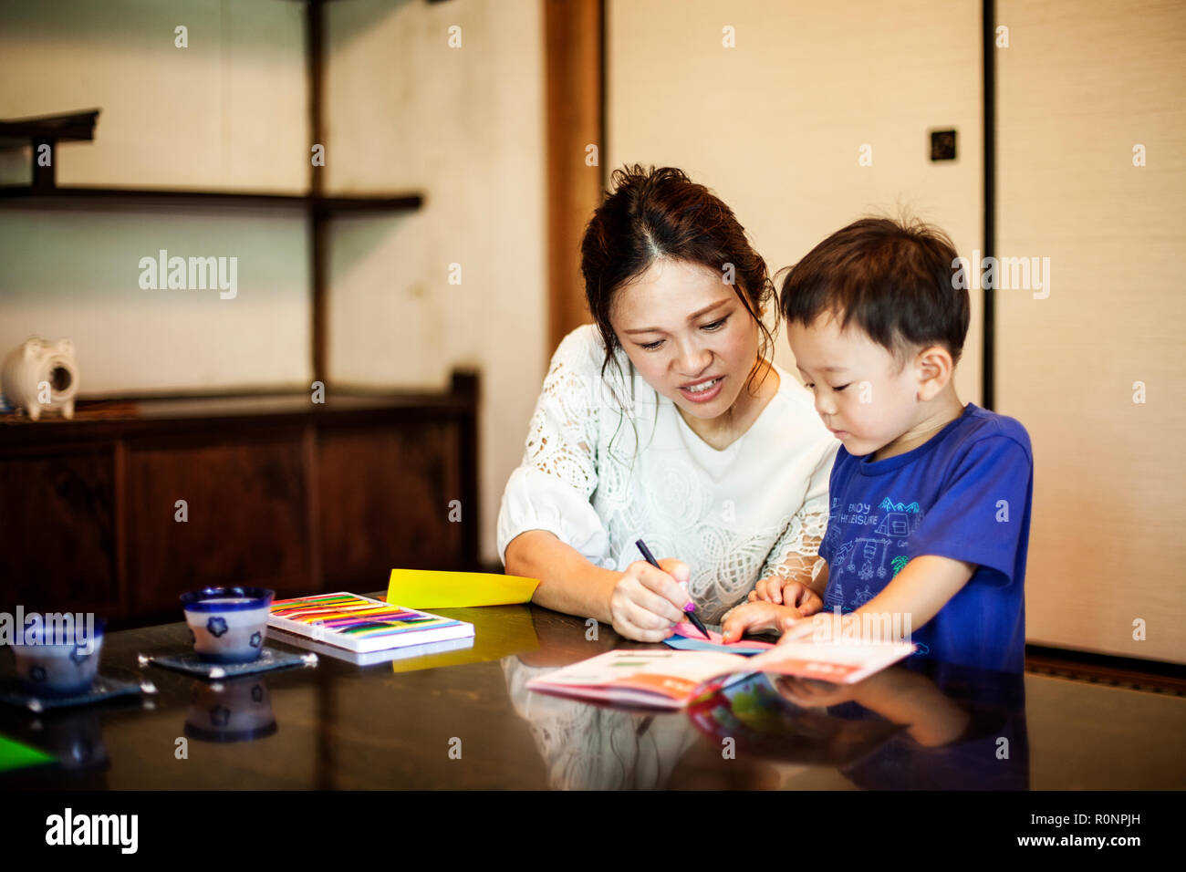 Japanese woman and little boy sitting at a table, drawing with colouring pens. Stock Photo