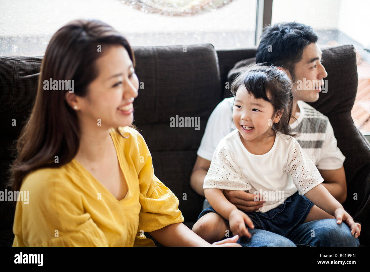 Portrait of smiling Japanese man, woman and young girl sitting on a sofa. Stock Photo