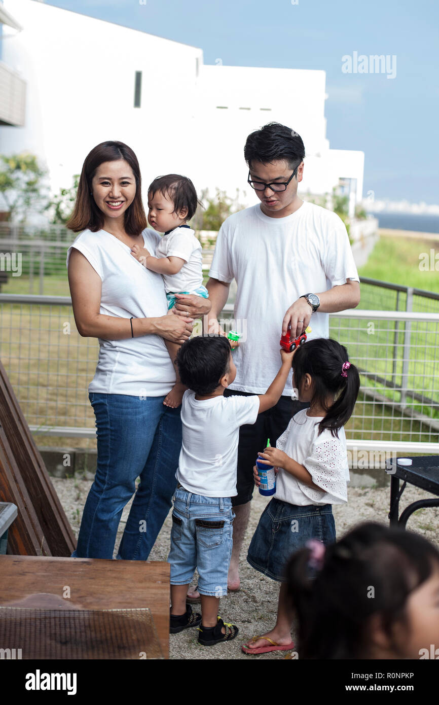 Portrait of smiling Japanese family with three young children standing in a back garden. Stock Photo