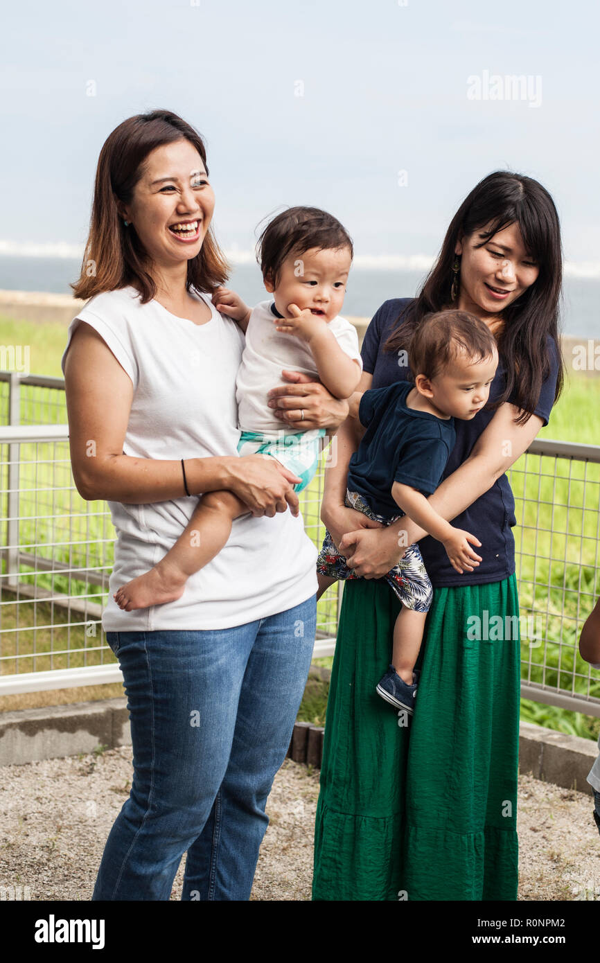 Portrait of two smiling Japanese women with two toddlers standing in a back garden. Stock Photo