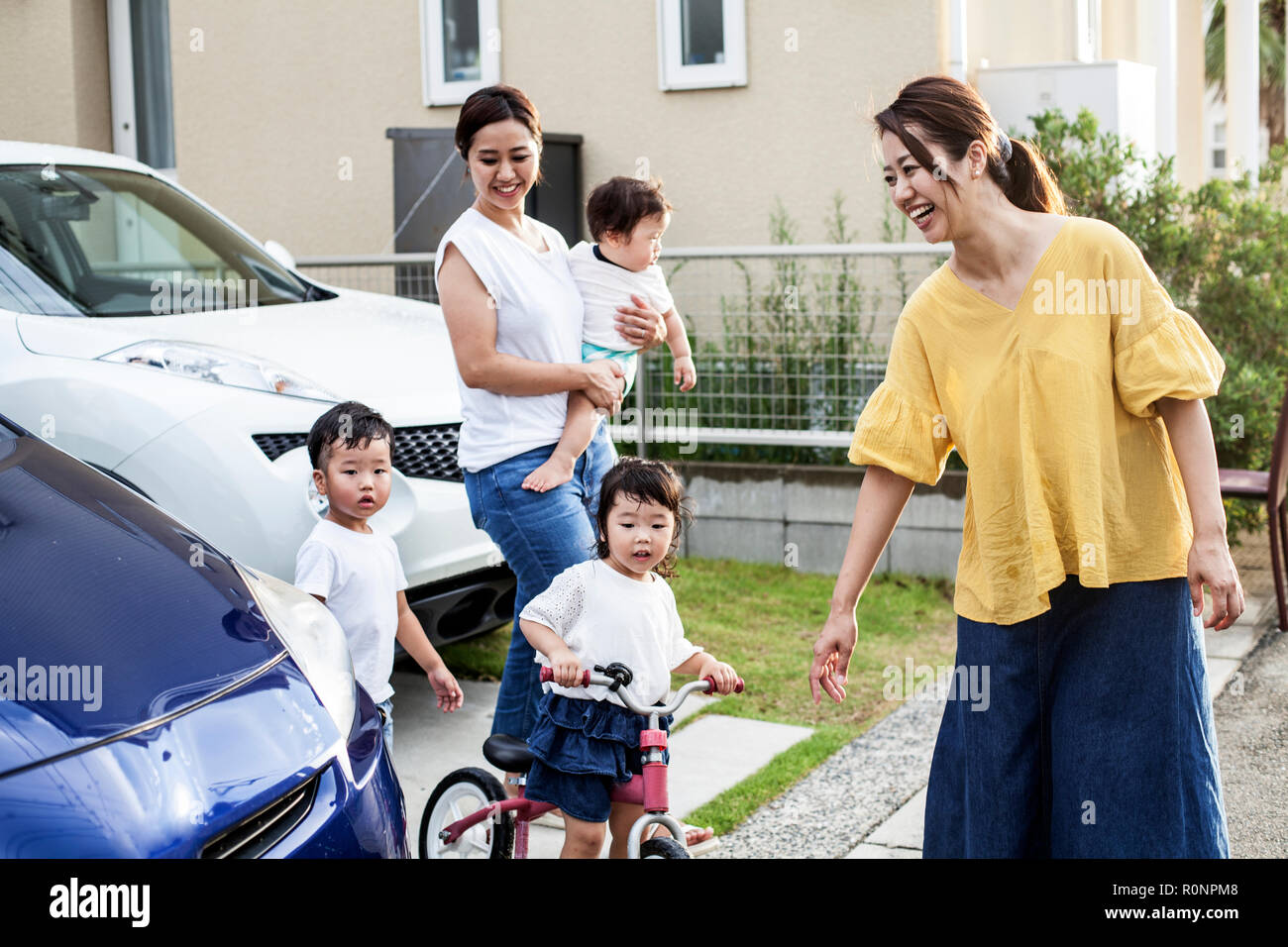 Two smiling Japanese women and three young children standing next to parked car in a street. Stock Photo