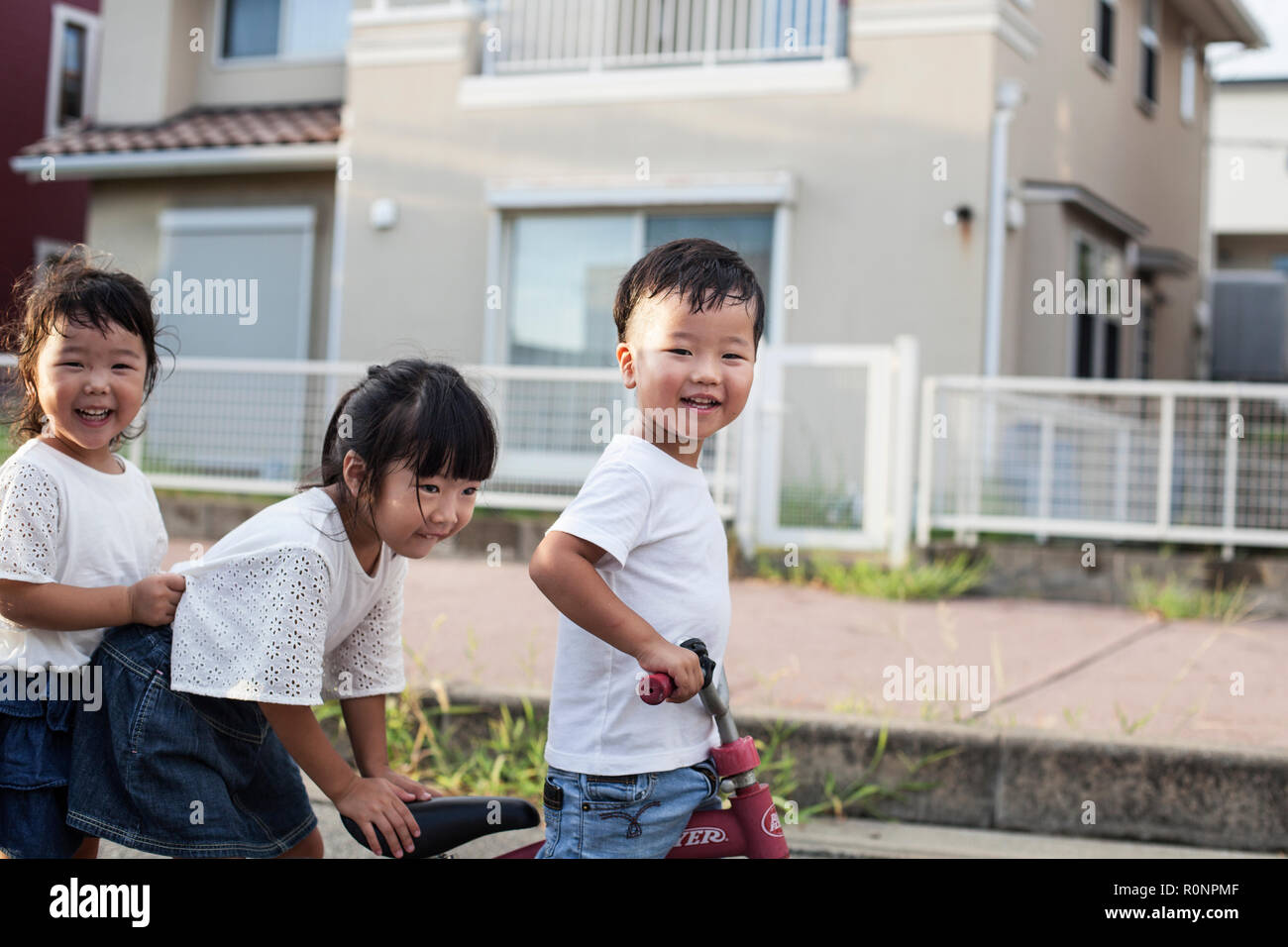 Portrait of two Japanese girls and boy playing on street with a bicycle, smiling at camera. Stock Photo