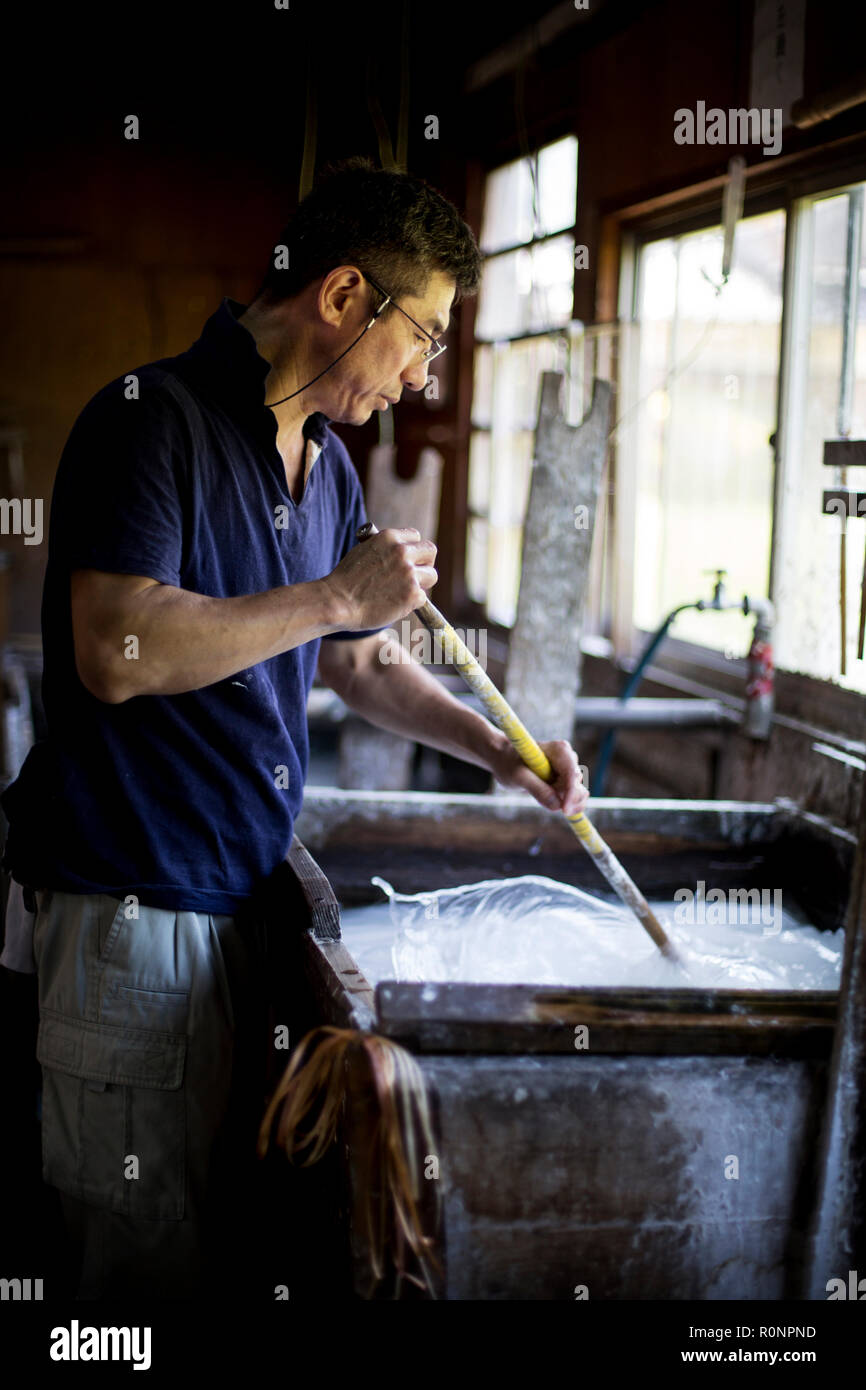 Japanese man stirring a vat of liquid in a with a stick