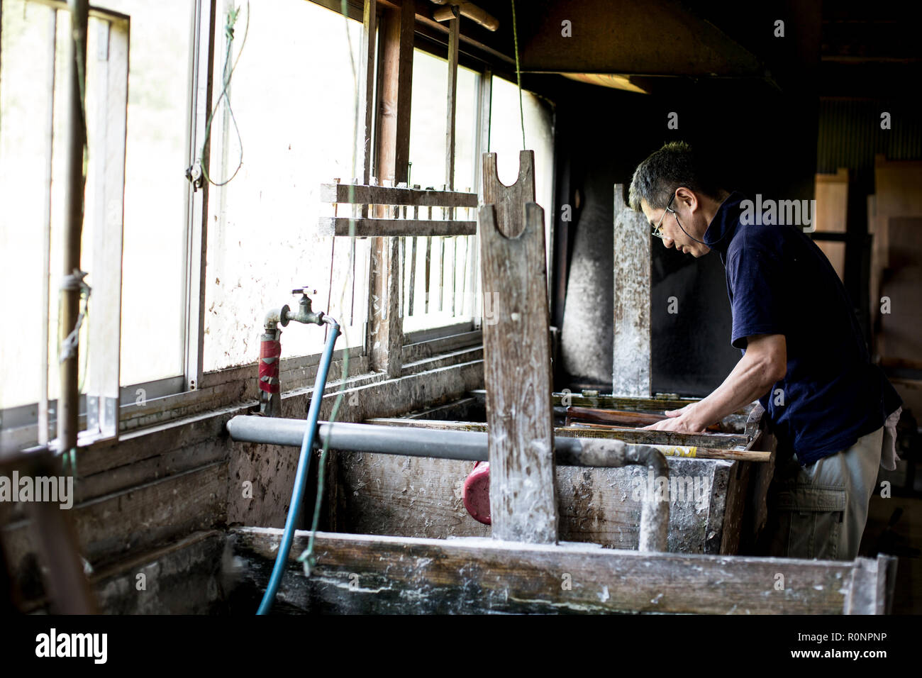 Japanese man in a leaning over a vat of liquid, the traditional Washi papermaking