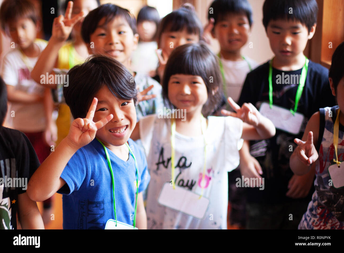 Group of smiling children in a Japanese preschool, making peace sign, looking at camera. Stock Photo