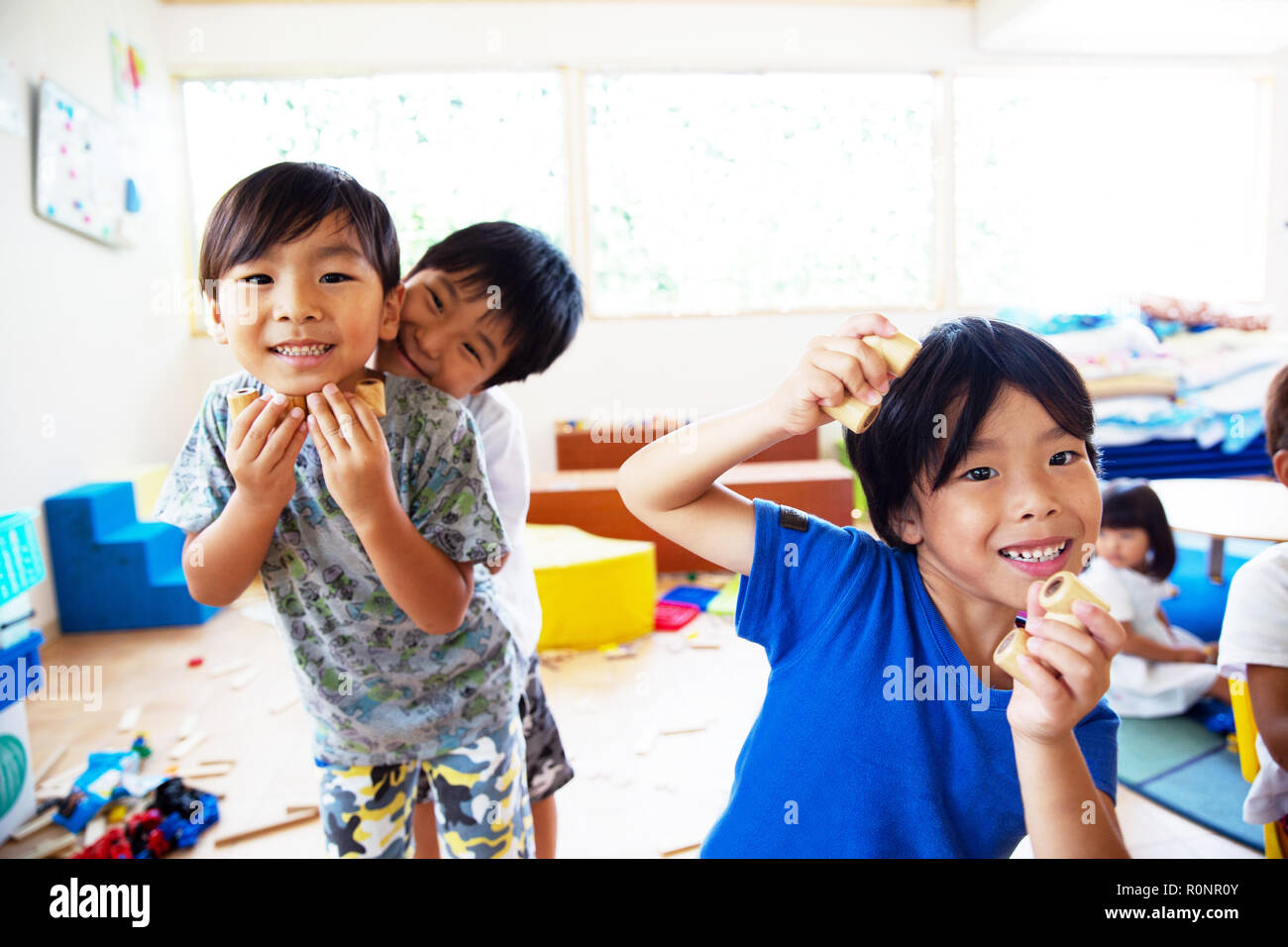 Three young children in a Japanese preschool, looking at camera and pulling faces,smiling. Stock Photo