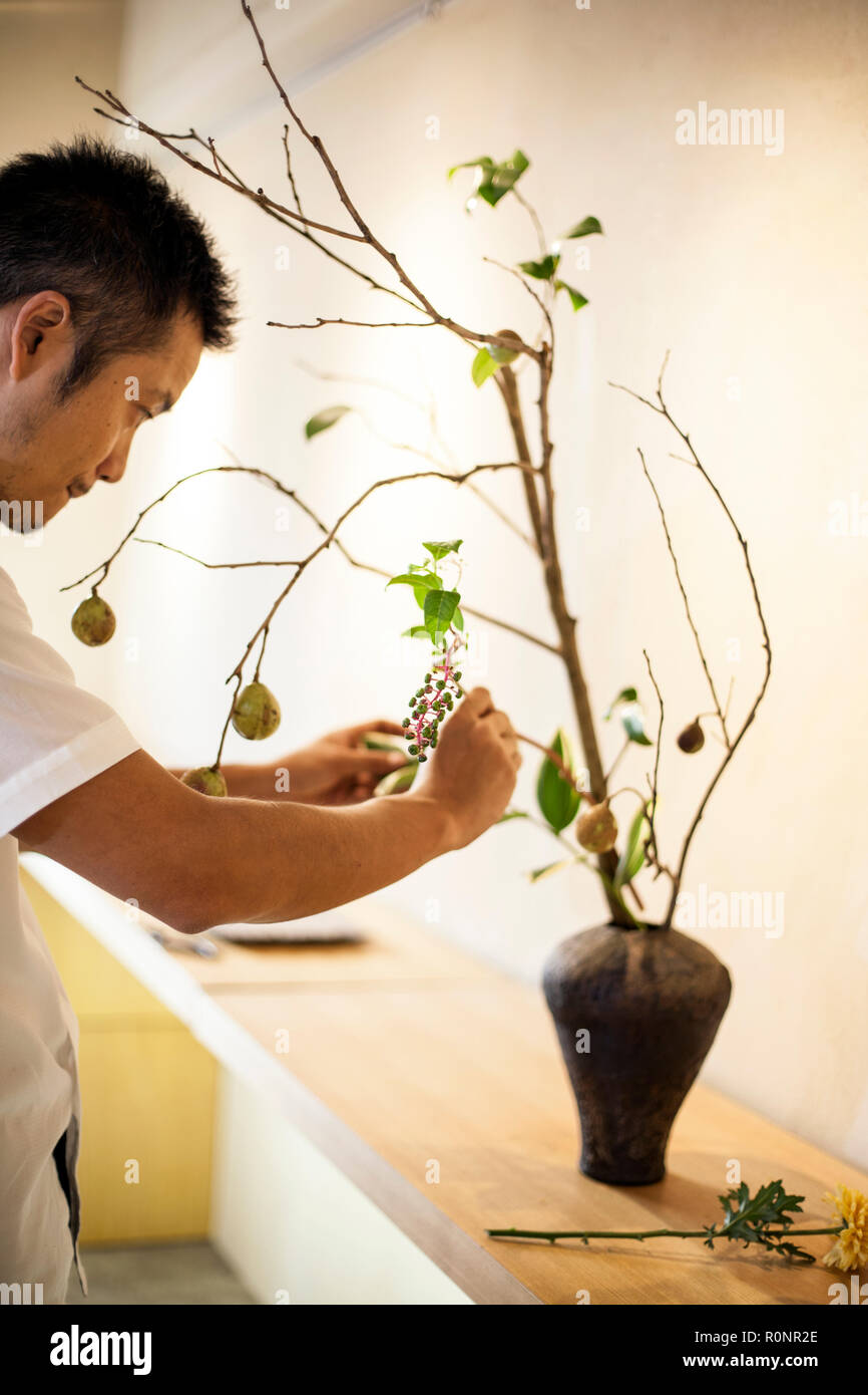 Japanese man standing in flower gallery, working on Ikebana arrangement