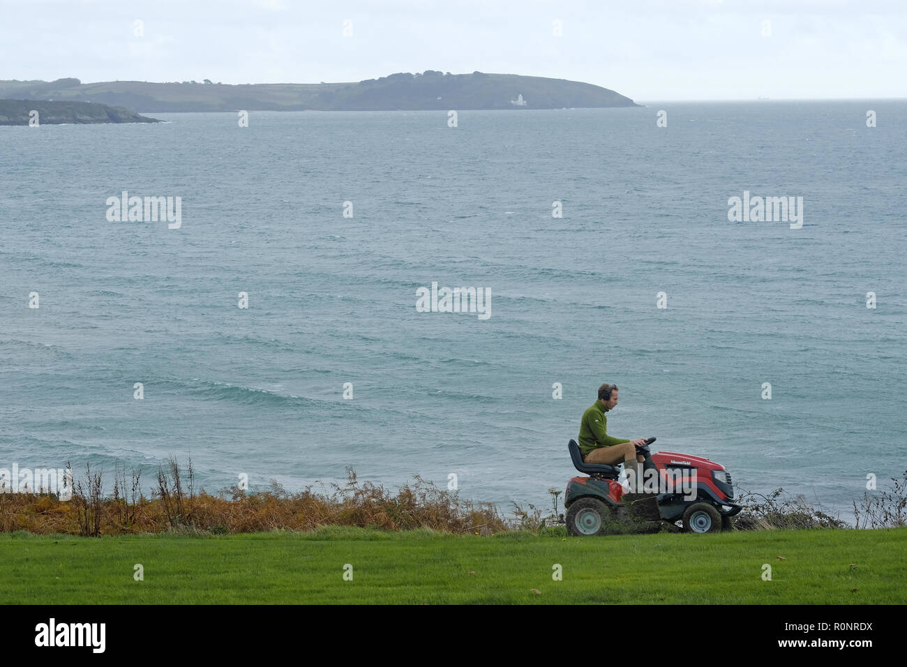 A man mowing a lawn by the sea in Cornwall. Stock Photo