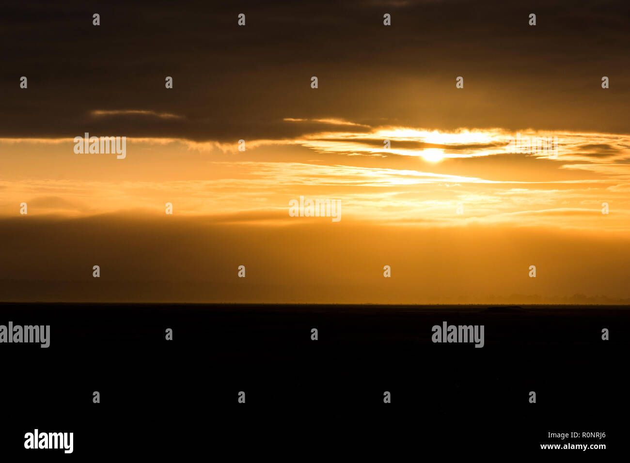 Bright dawn at Mont-Saint-Michel Bay, France, with a black horizon and an orange sky Stock Photo