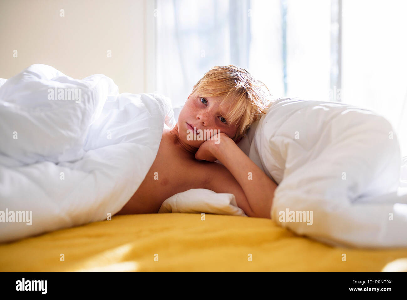 Boy lying in bed leaning on his elbow Stock Photo