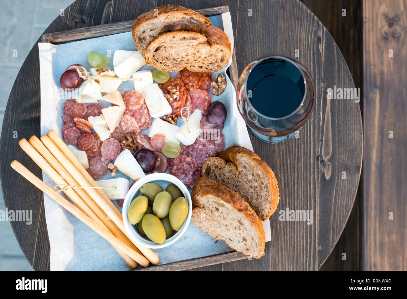 Overhead view of cheese, charcuterie, olives, grapes and bread on a table with a glass of red wine Stock Photo