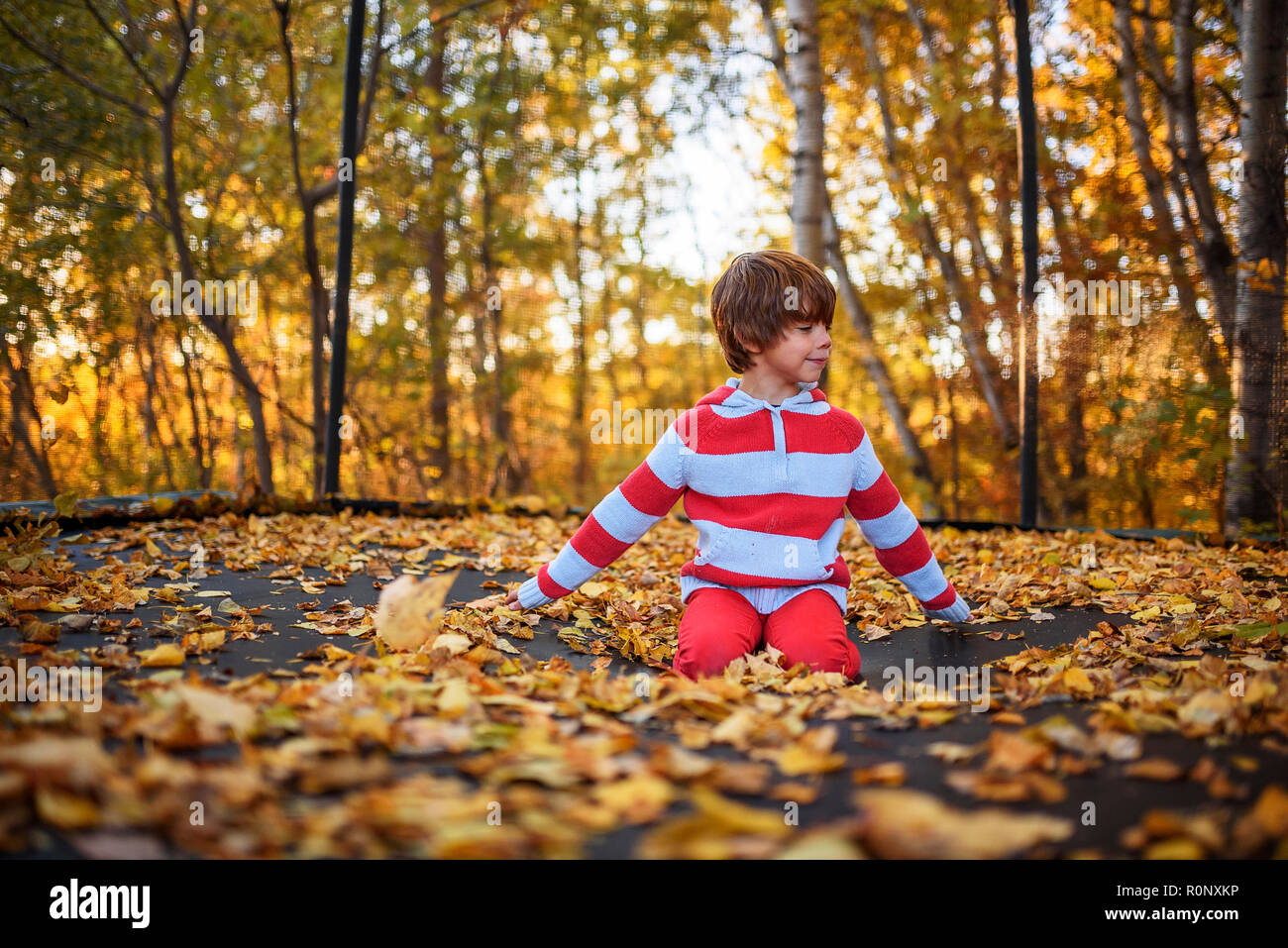 Boy sitting on a trampoline covered in autumn leaves, United States