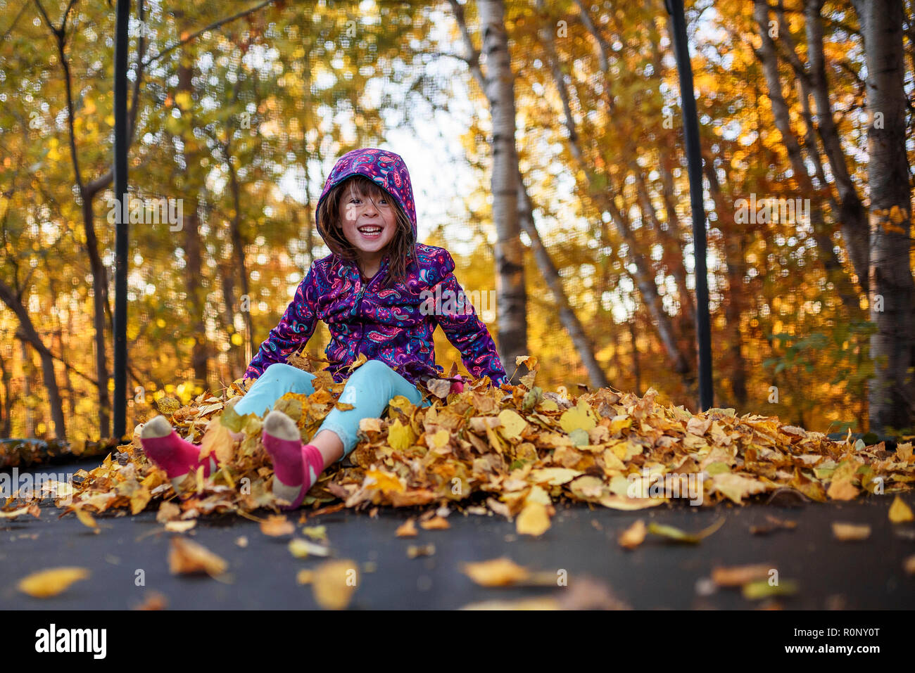Smiling girl sitting on a stack of autumn leaves on a trampoline, United States Stock Photo