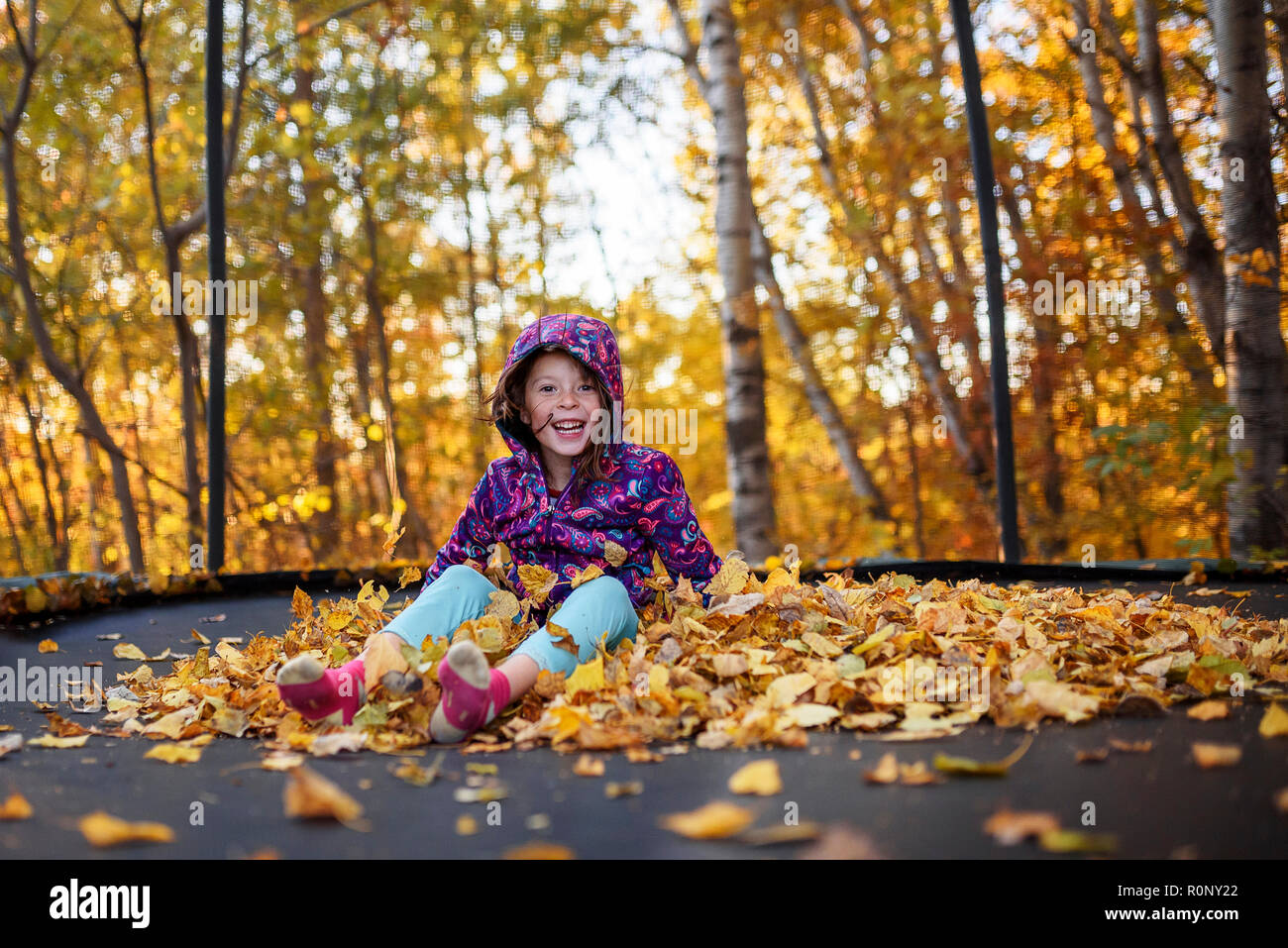 Smiling girl sitting on a stack of autumn leaves on a trampoline, United States Stock Photo