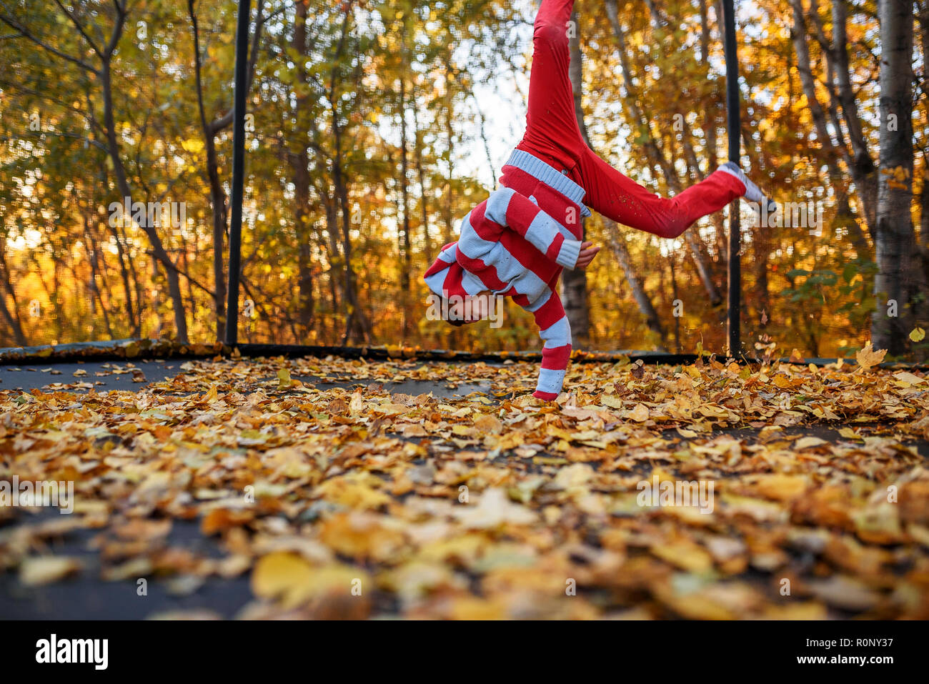 Boy jumping on a trampoline covered in autumn leaves, United States