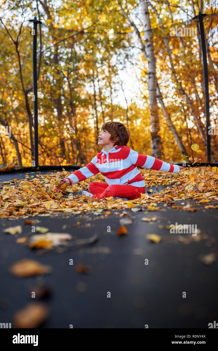 Boy sitting crosslegged on a trampoline covered in autumn leaves