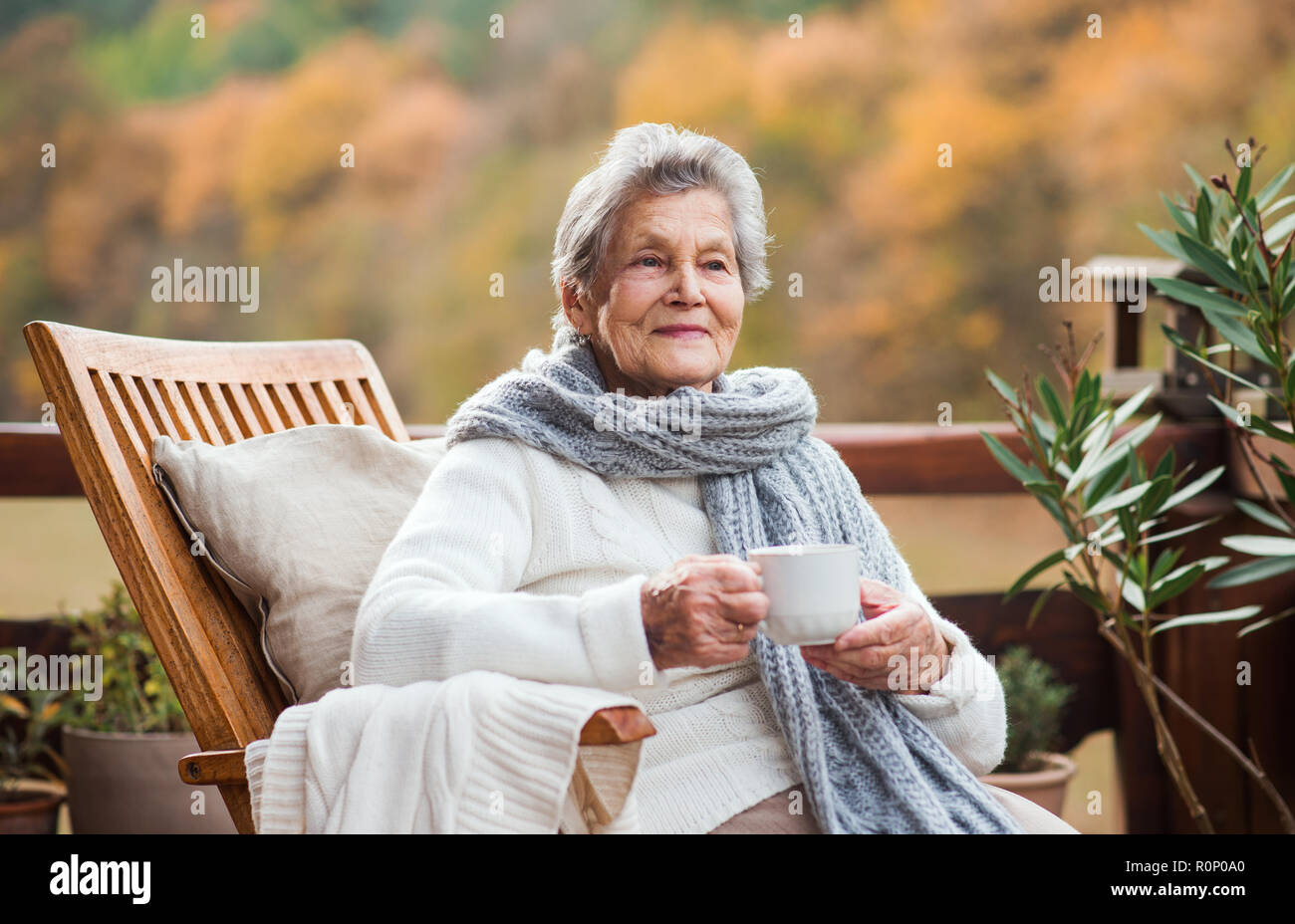 An elderly woman sitting outdoors on a terrace in on a sunny day in ...
