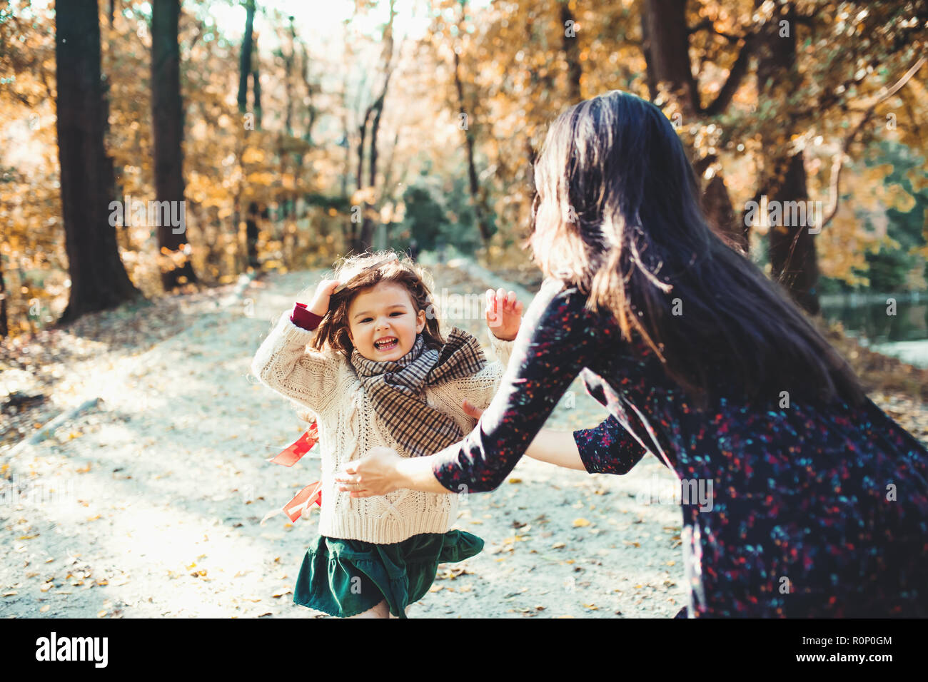 A young mother with a toddler daughter running in forest in autumn nature. Stock Photo