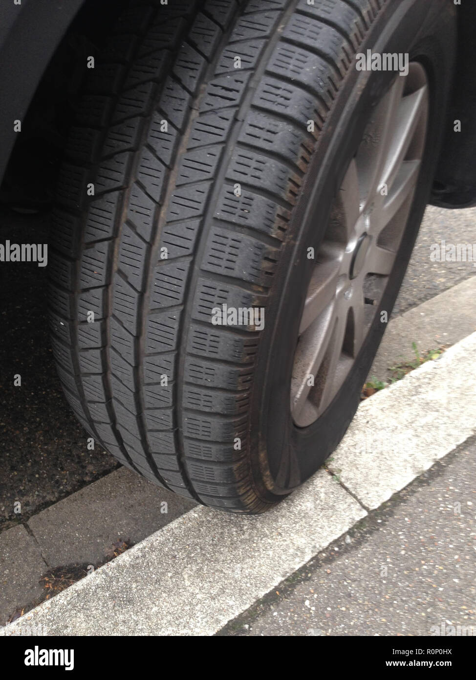 Auto parkt nur halb auf der Bordsteinkante, der Reifen hängt halb in der Luft, und rutscht langsam ab Stock Photo