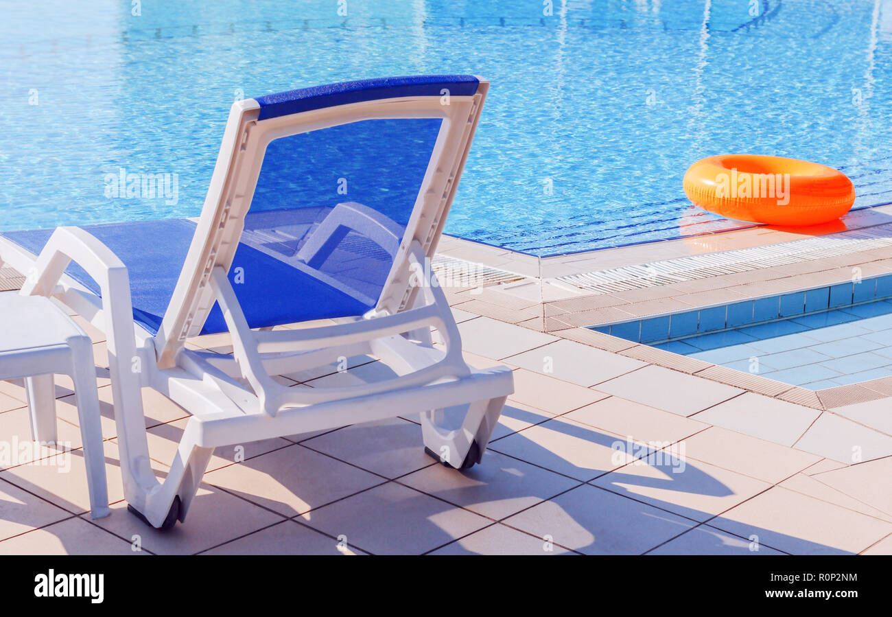 White blue sunbed by pool with light blue water at sunny day Stock Photo