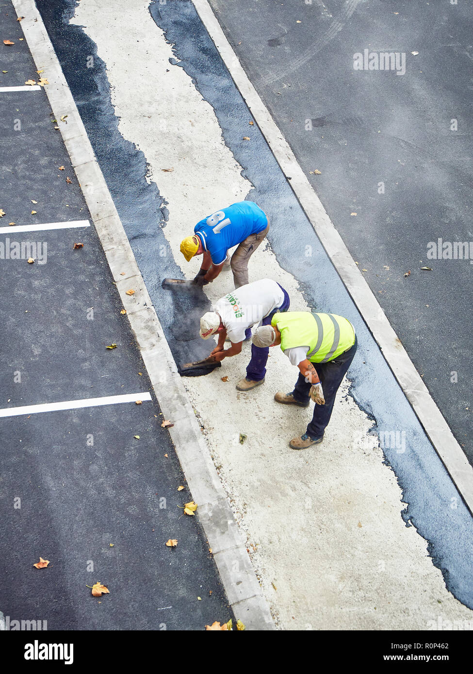 Laborers applying manually fresh asphalt during the making of a pedestrian path. Stock Photo