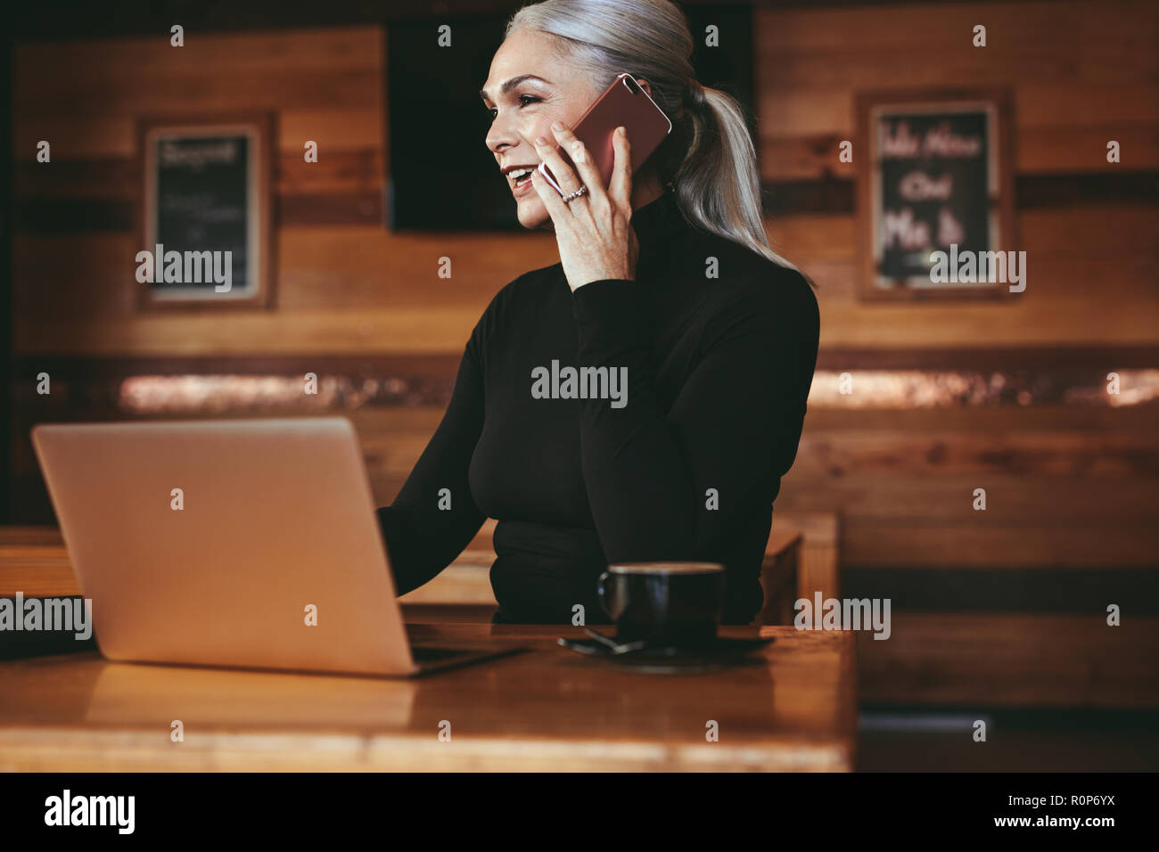 Beautiful senior businesswoman sitting at cafe having telephonic conversation with client. Mature female business professional talking on mobile phone Stock Photo
