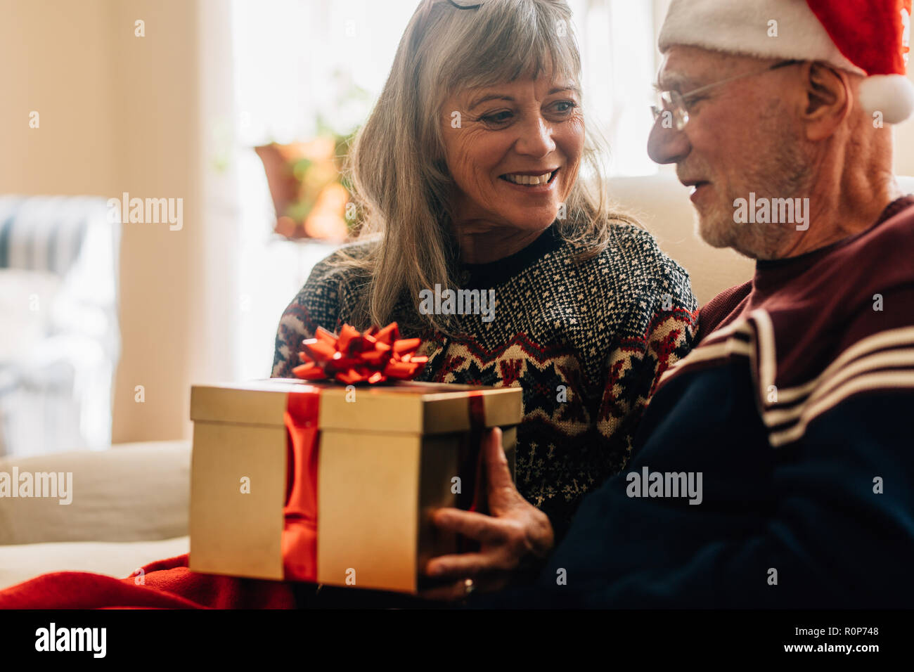 Elderly woman giving a gift to her husband for christmas. Senior couple exchanging gifts celebrating christmas at home. Stock Photo