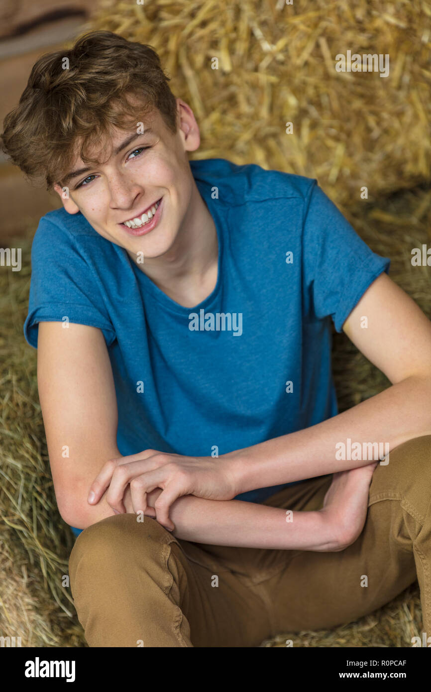 Young man happy smiling laughing male boy teenager sitting on hay bales in a barn Stock Photo