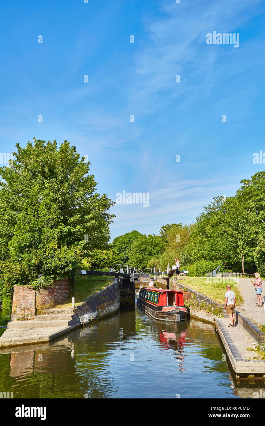 A red painted barge on the Kennet and Avon canal with people looking on just after passing through a lock on a sunny day, Newbury, Berkshire, UK Stock Photo