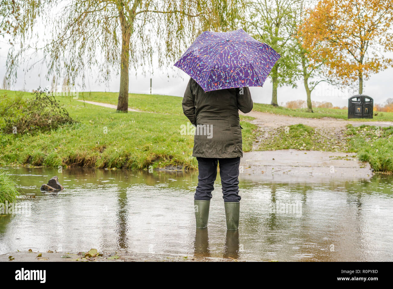 Kidderminster, UK. 7th November, 2018. UK weather: with today's persistent heavy showers (coupled with the significant overnight downpour), water levels are on the rise in Worcestershire with some areas experiencing flash flooding. A woman wearing wellies and holding an umbrella stands outdoors, rear view, isolated in rising water. Credit: Lee Hudson/Alamy Live News Stock Photo