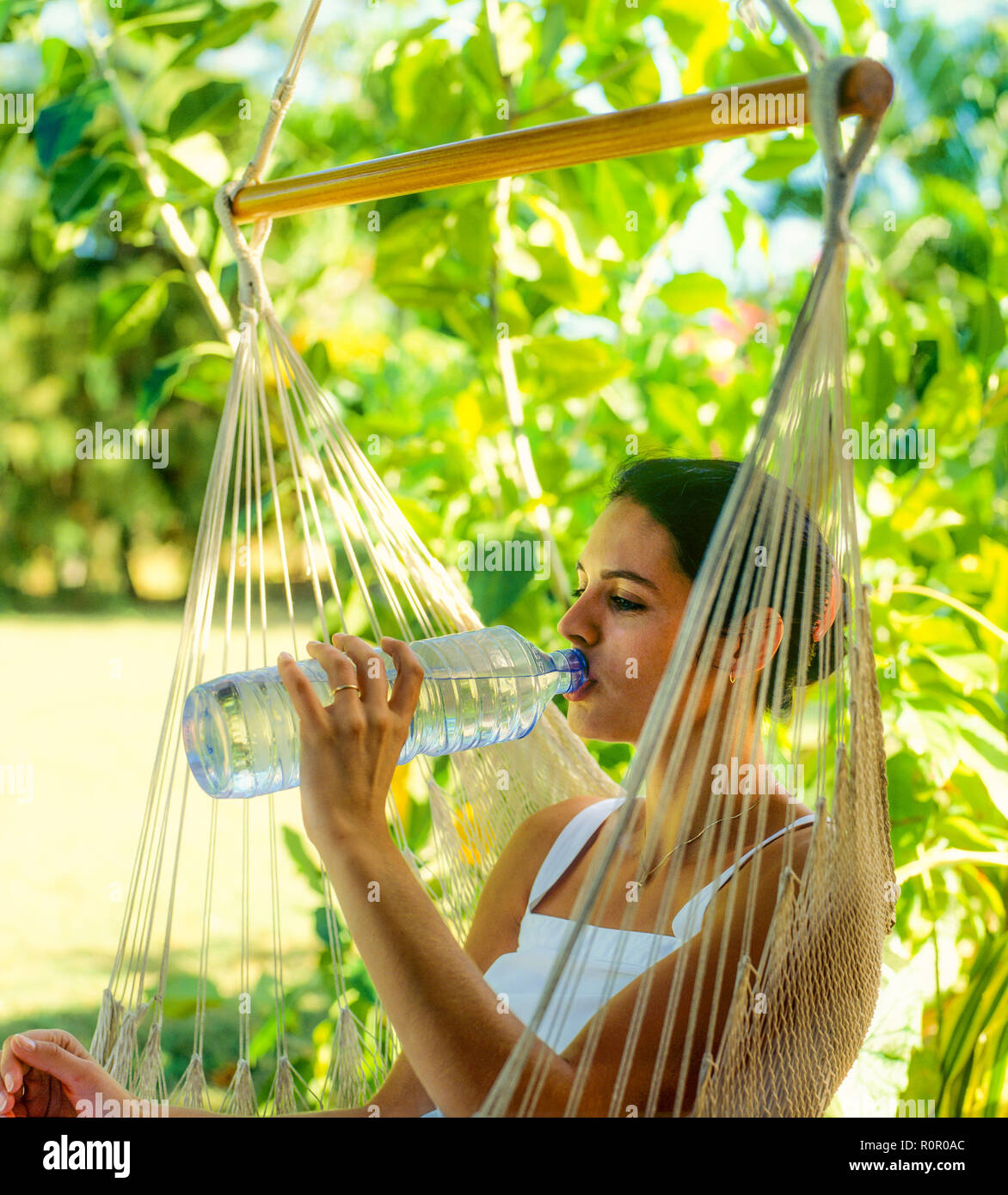 Young woman drinking mineral water from plastic bottle, tropical garden, Guadeloupe, French West Indies, Stock Photo