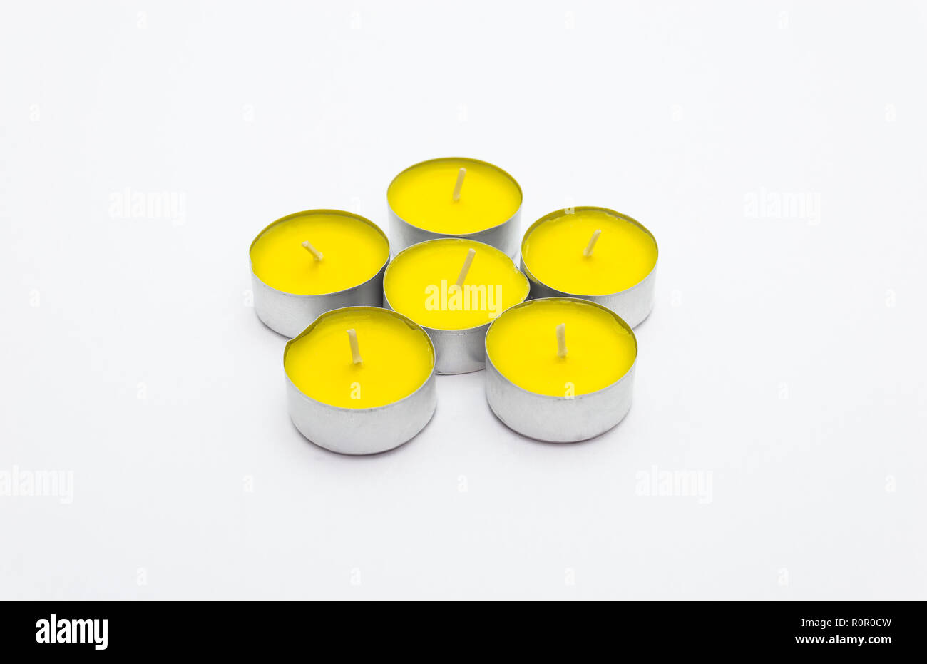 A set of yellow tealight paraffin candle lies on a white background