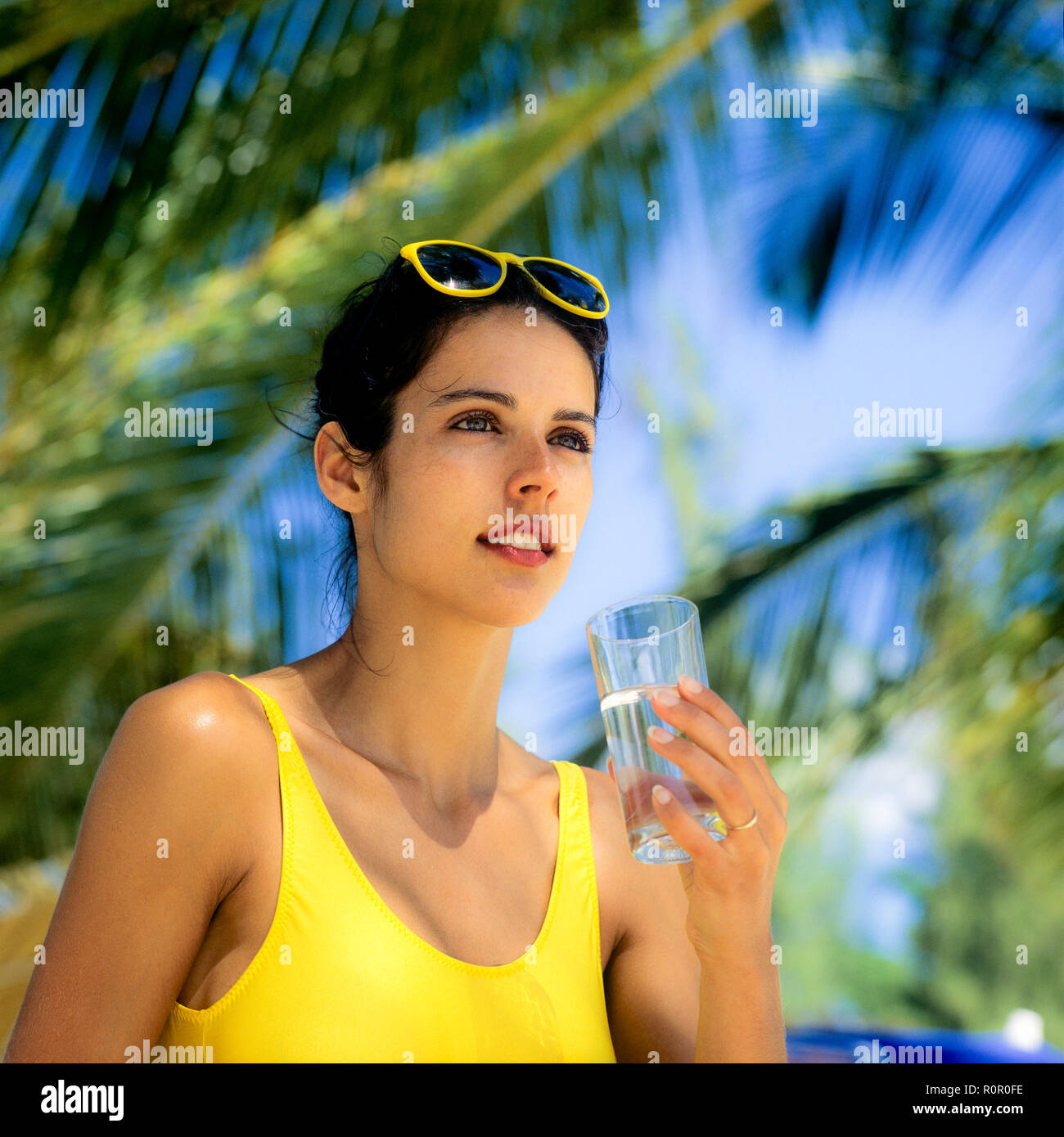 Young woman with yellow swimsuit holding a glass of water, palm trees background, Guadeloupe, French West Indies, Stock Photo