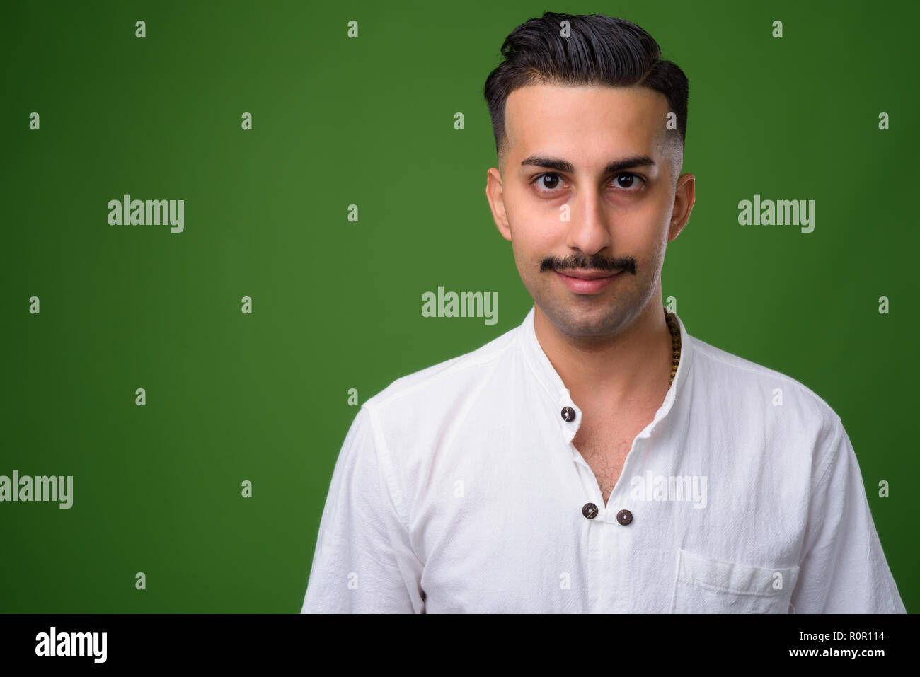 Young handsome Iranian man with mustache against green backgroun Stock Photo