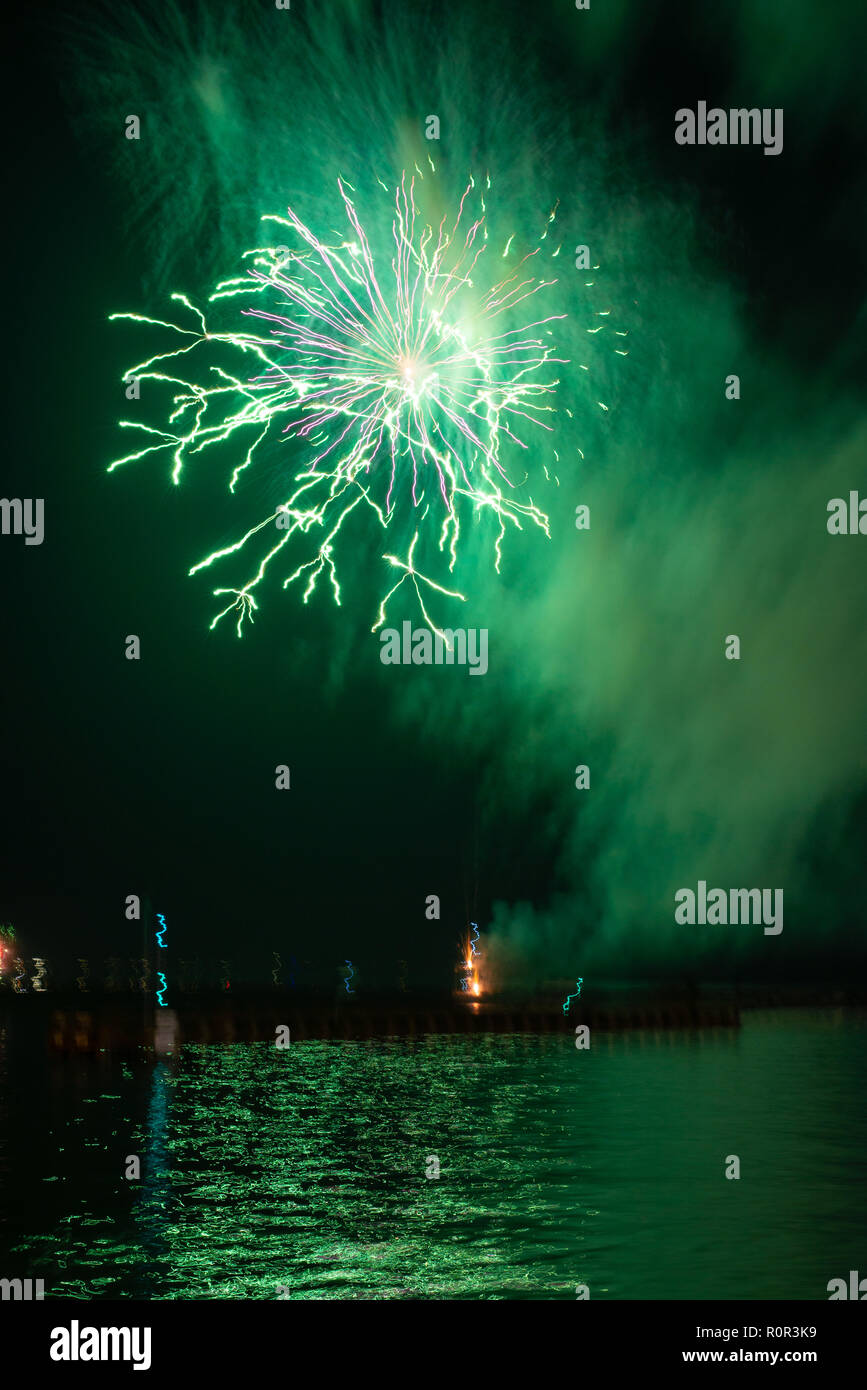 Long exposure, hand held shot of a green rocket firework bursting over the sea with streaky light and snowflake like patterns from the explosion. Stock Photo