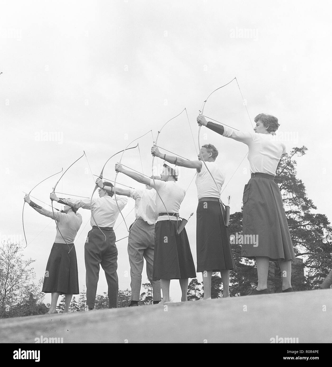 Archery in the 1950s. A group of men and women are standing with their bows and arrows, aiming at a target. Sweden 1957. Photo Kristoffersson Ref BY47-6 Stock Photo