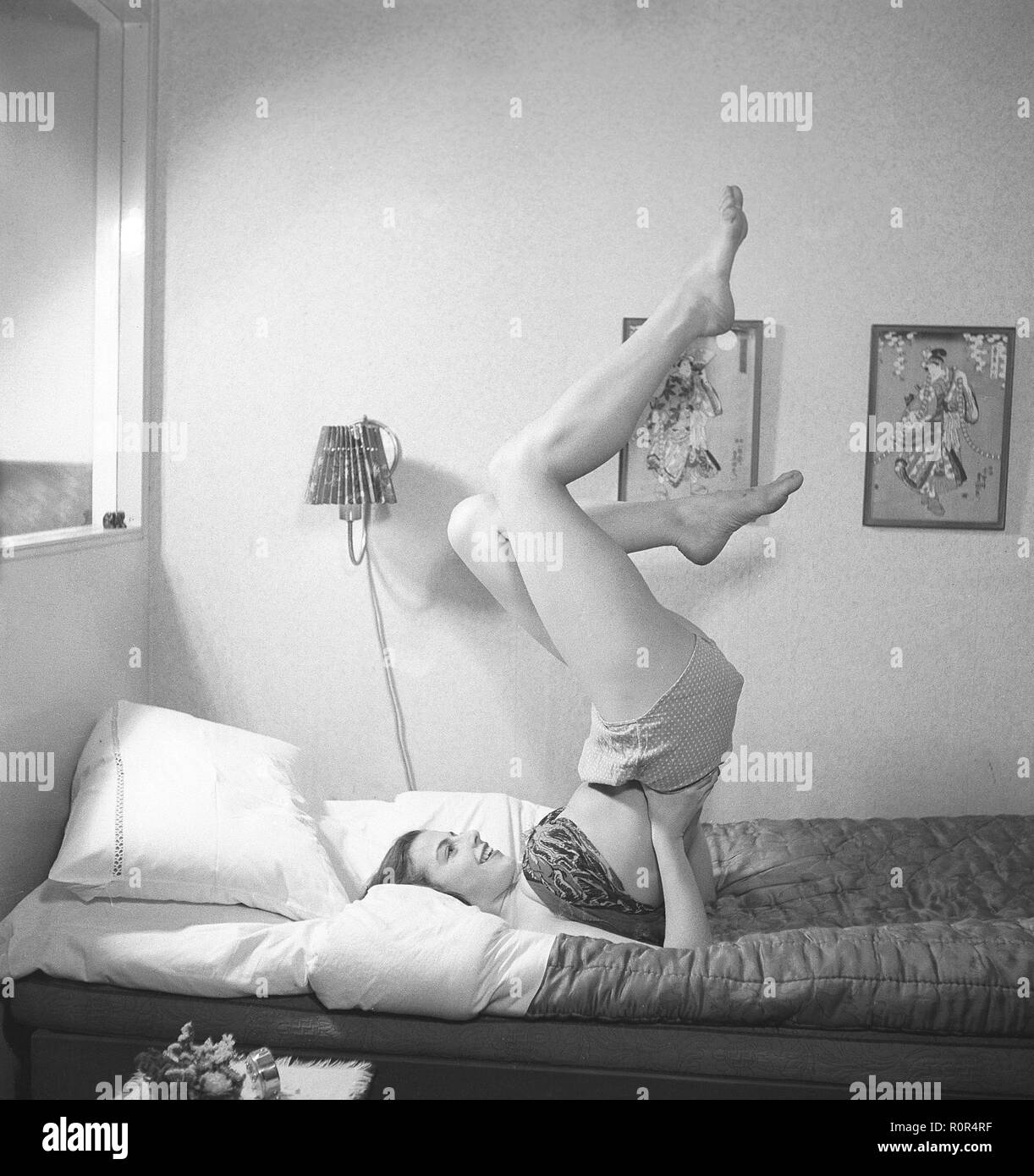 Morning exercise in the 1940s. A young woman is lying in bed and holding her legs up while moving around to get the in shape for the day.  Sweden 1946. Photo Kristoffersson ref Y22-1 Stock Photo