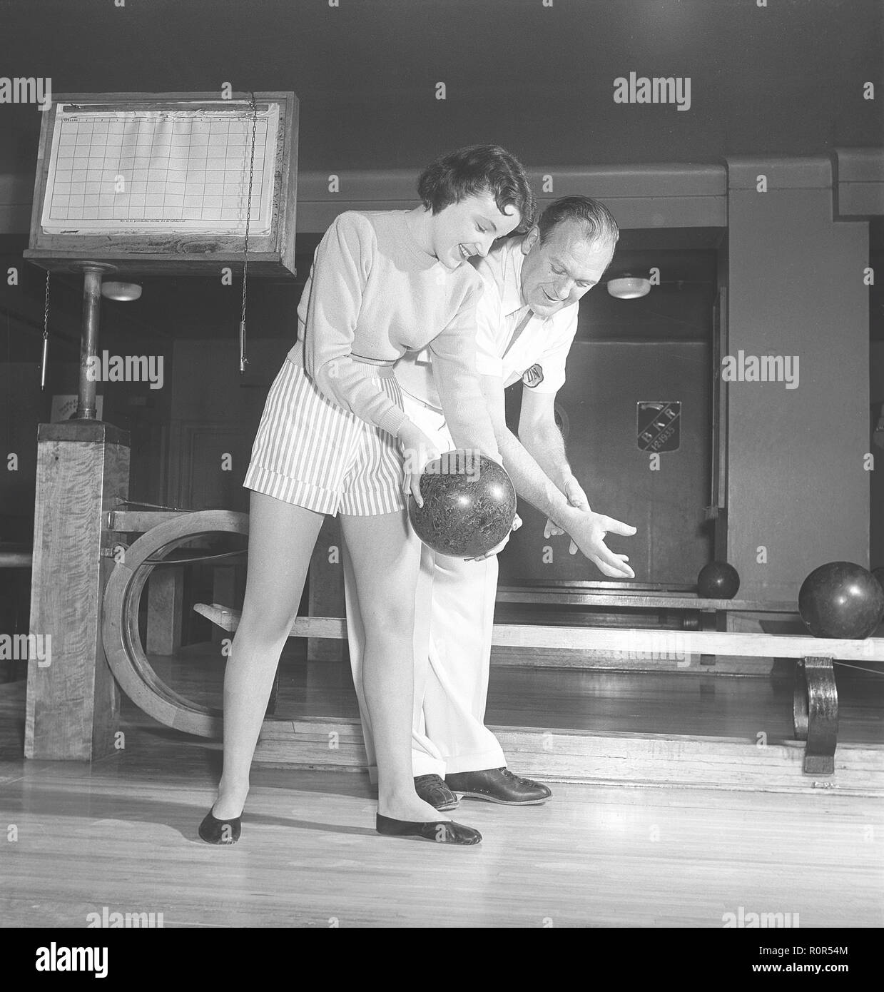 Bowling in the 1950s. A man with three young women in a bowling alley. They are dressed in short striped skirts and jumpers. The three girls are all theatre actresses; Ingrid Björk, UllaCarin Rydén and Brita Ulfberg. Ewert Ekström shows is instructing them in bowling. He was a professional bowler player in the 1930s and is at this time an instructor and owner of the bowling club.  1950. Sweden Photo Kristoffersson ref AY36-12 Stock Photo