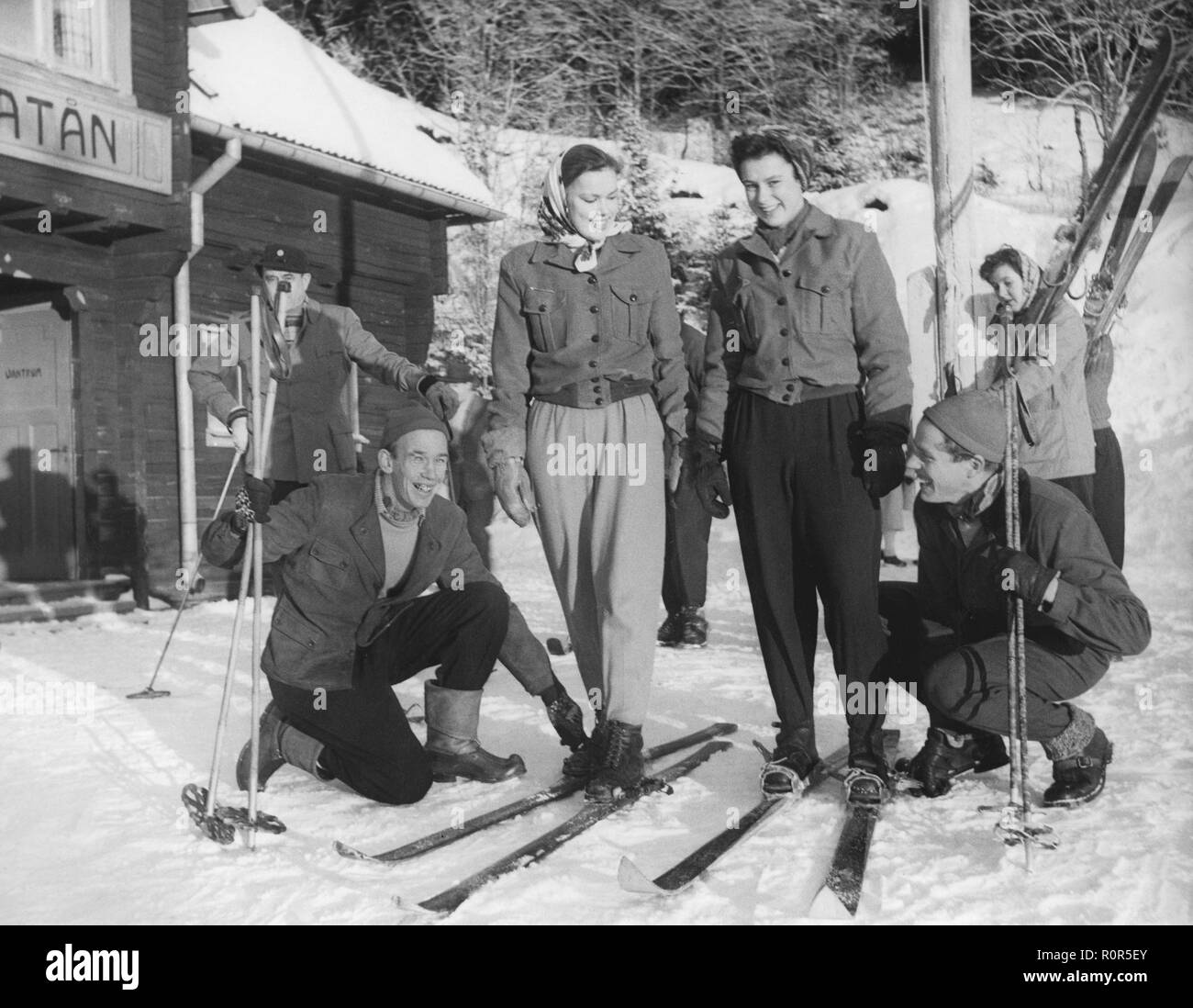 Winter in the 1940s. A young couple on ski holiday gets help to fasten their skis by world record skier Stig Lindgård and long distance runner Roland Sundin. Åre Sweden 1947 Stock Photo