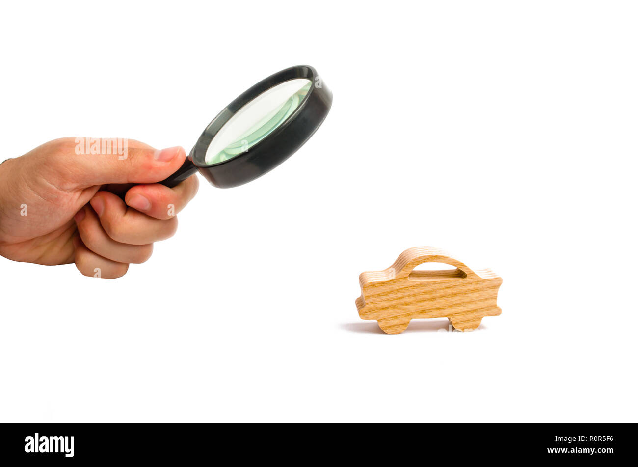 Magnifying glass is looking at the Wooden figurine of a car on a white background. Minimalism. The concept of car insurance, buying and selling cars.  Stock Photo