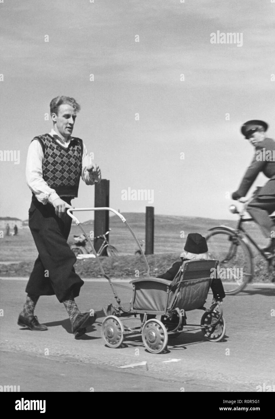 Father and child in the 1940s. A man wearing typical 1940s trouser fashion is pushing a stroller with his child in it. He is marching for a charity event 1942 Stock Photo