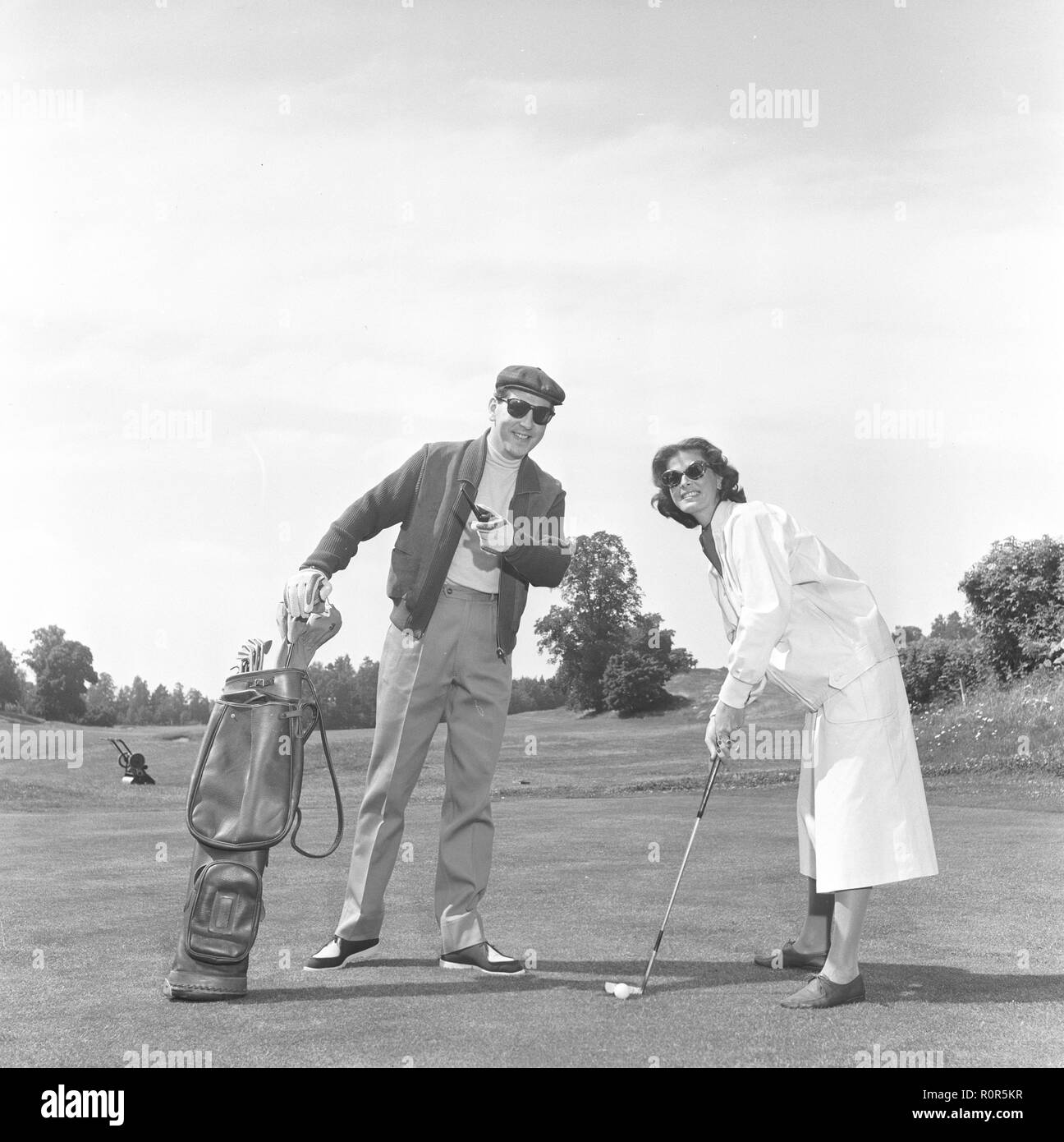 Fashion and golf in the 1950s. A couple playing golf wearing this years latest fashion. She is wearing a whit jacket and white wide legged trousers. He has a short sports jacket and nicely pressed trousers. Sweden 1957 Stock Photo