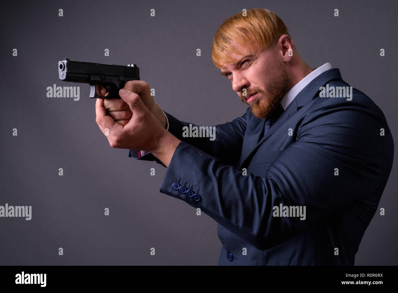 Bearded businessman with handgun against gray background Stock Photo