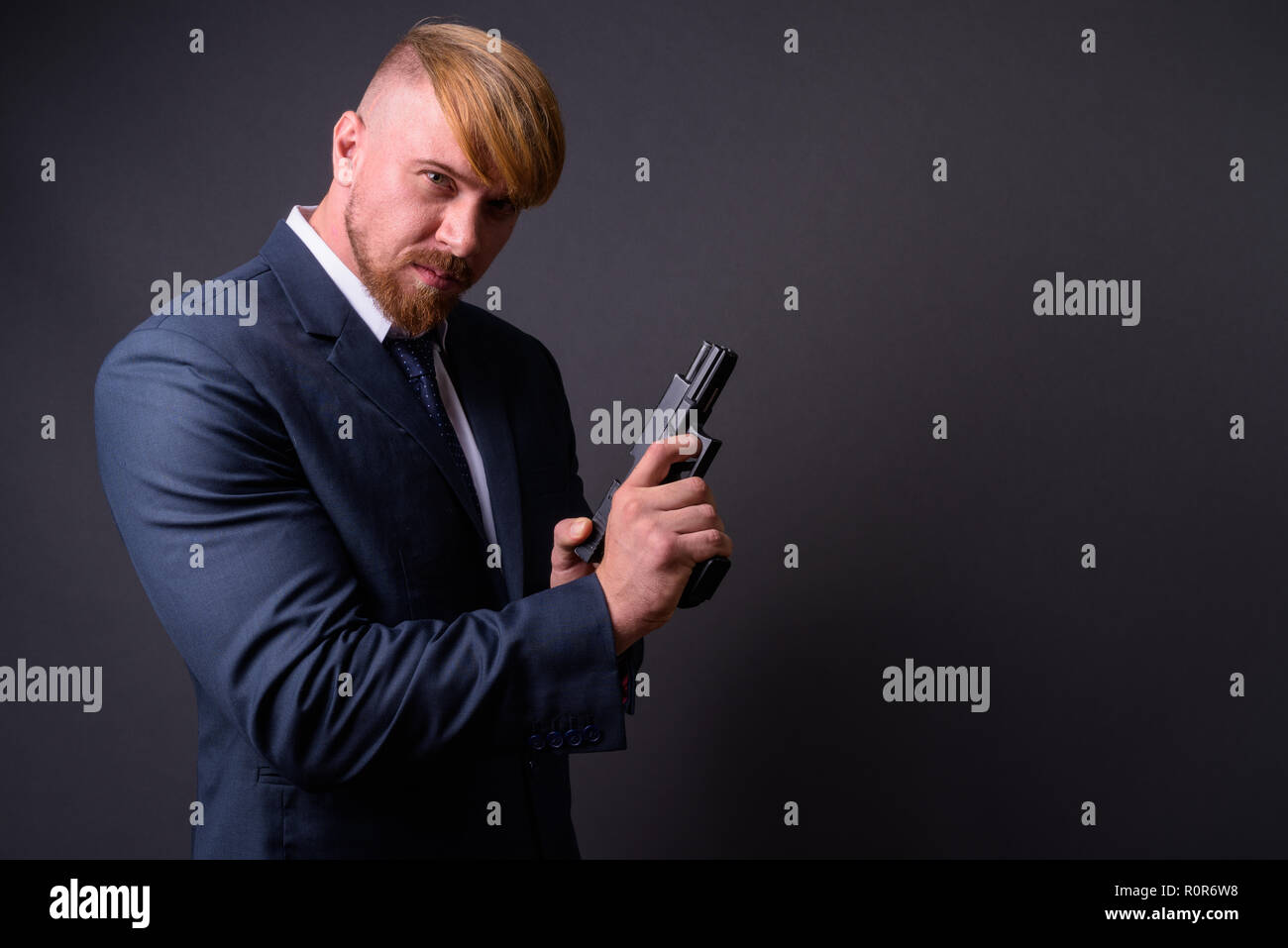 Bearded businessman with handgun against gray background Stock Photo
