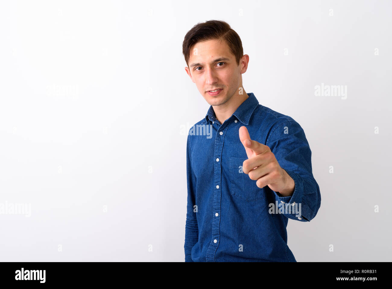Studio shot of young handsome man pointing at camera against whi Stock Photo