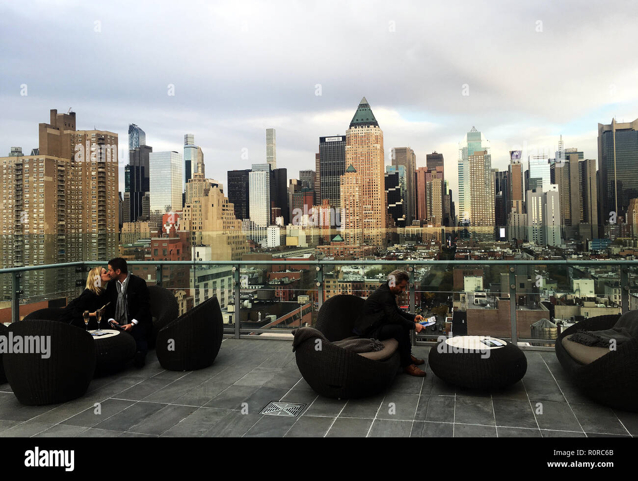 Young professional couple share a kiss and champagne at Press Lounge rooftop bar in front of the Manhattan skyline in early evening, New York, NY Stock Photo