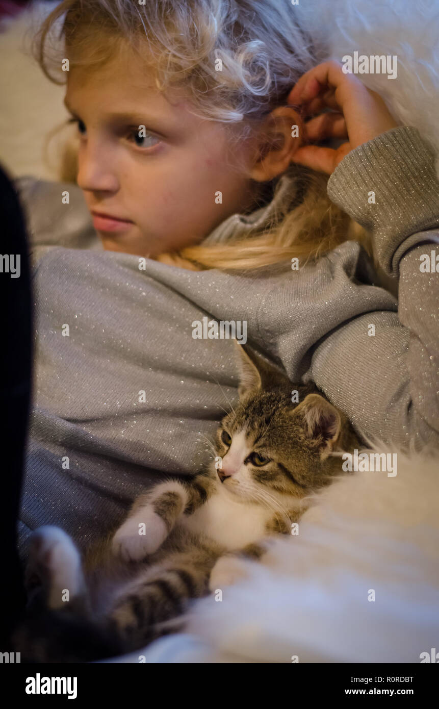 lovely blond girl and cute cat relaxing lying on sofa and watching television Stock Photo