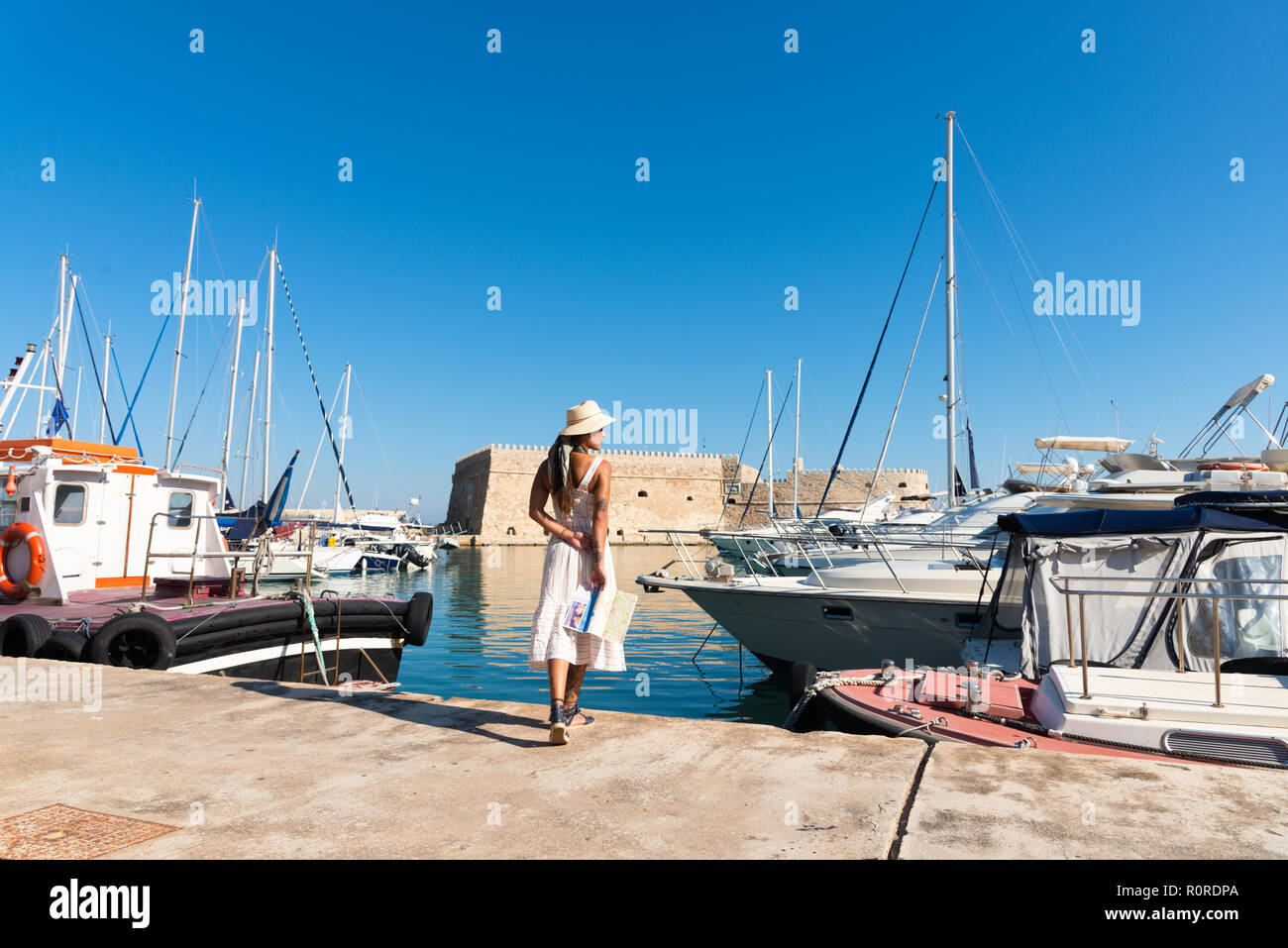 Traveling tourist woman on vacation in Heraklion Crete walking at the port. Lovely elegant girl in beige dress visiting the famous Mediterranean Venet Stock Photo