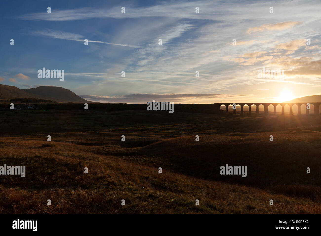 A Northern rail class 158 sprinter train passing between Ribblehead viaduct and Ingleborough in the Yorkshire dales at sunset making a silhouette Stock Photo