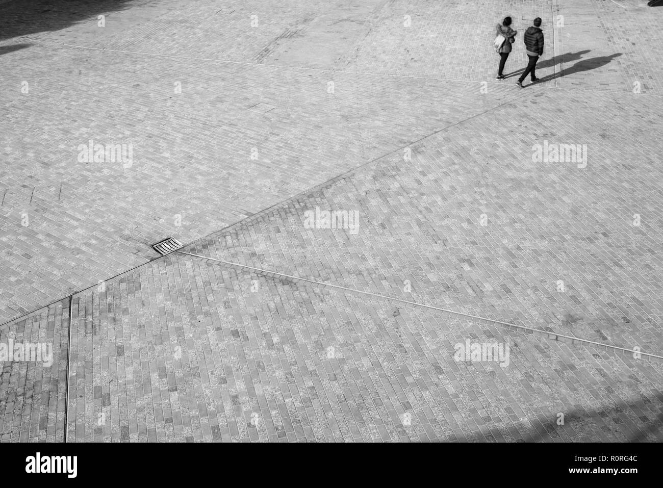 Blurred unrecognizable people from above walking on an open space square with shadows projecting on the floor Stock Photo